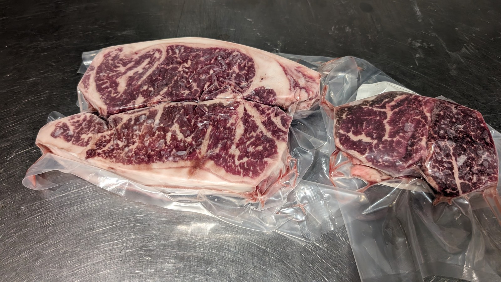 Vacuum-sealed beef steaks on a stainless steel table, marbled through the cut