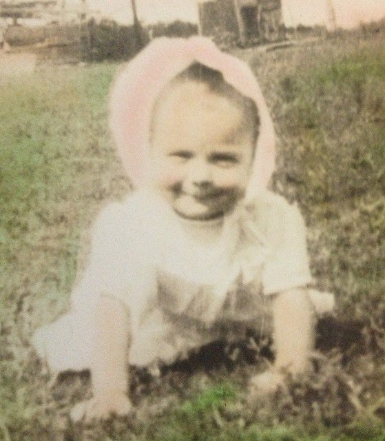 A baby in a bonnet sitting on the grass, an old colour print.