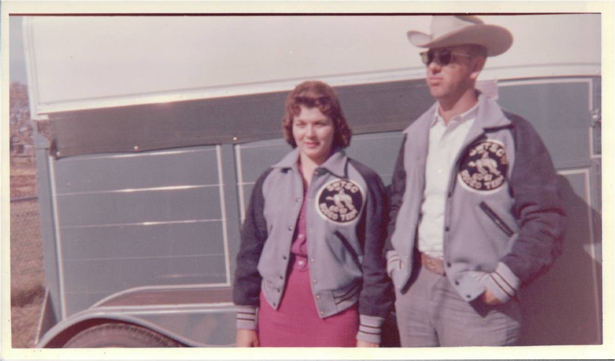 A young woman and a young man in matching jackets beside a stock trailer.