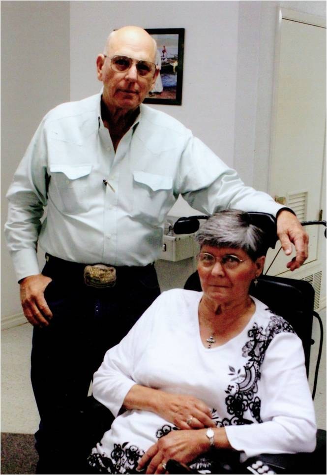 A man standing behind a seated woman in a black and white blouse.